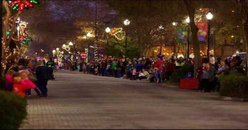 A festive street lined with people enjoying holiday lights and decorations during an evening event.