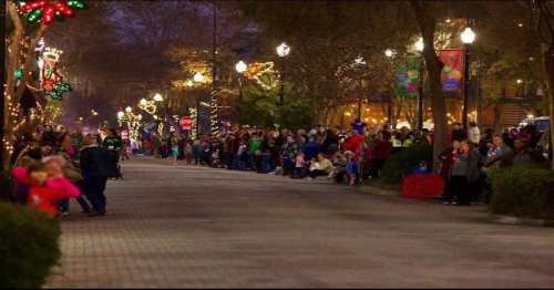 A festive street lined with people enjoying holiday lights and decorations during an evening event.