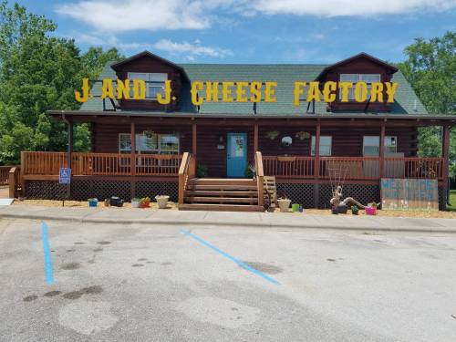 A log cabin-style building with a sign reading "J and J Cheese Factory" and a welcoming entrance.