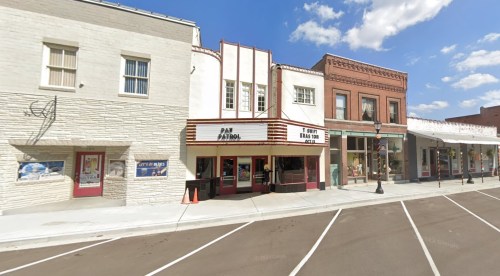 Historic theater building with marquee, flanked by brick storefronts under a blue sky with scattered clouds.
