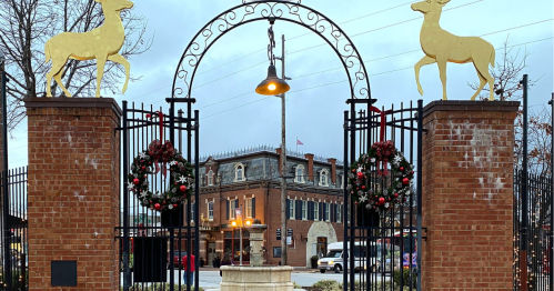 A decorative archway with deer sculptures and holiday wreaths, leading to a historic building in the background.