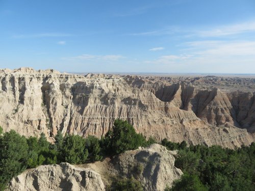 A panoramic view of rugged, layered rock formations and green vegetation under a clear blue sky.