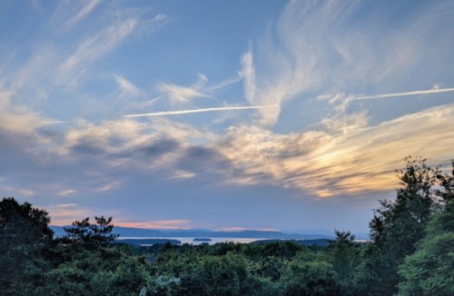 A serene sunset over a lake, with wispy clouds and silhouettes of trees in the foreground.