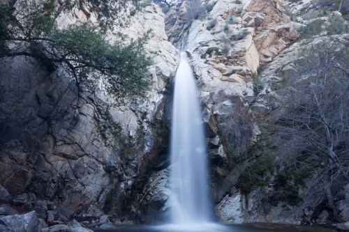 A serene waterfall cascading down rocky cliffs, surrounded by trees and natural vegetation.