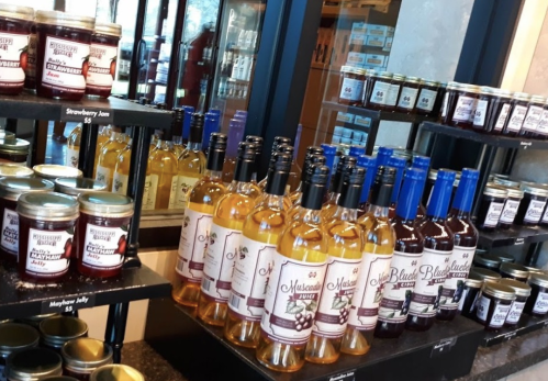 Bottles of wine and jars of jam displayed on shelves in a store, featuring various flavors like strawberry and blueberry.