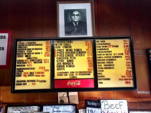 Menu board displaying various food items and prices, with a black-and-white photo of a man in a suit above it.
