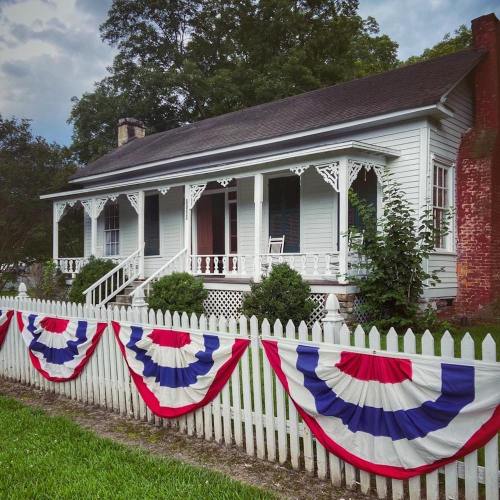 A charming white house with a porch, decorated with red, white, and blue bunting along a white picket fence.