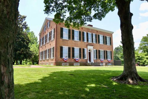 Historic brick building with large windows, surrounded by green grass and trees, decorated with red, white, and blue bunting.