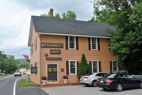A charming orange building with a sign reading "Bittersweet Shop of Gaylordsville," surrounded by greenery and parked cars.