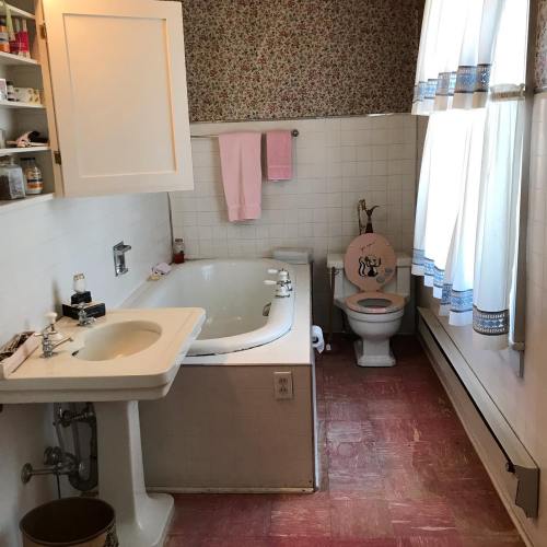A vintage bathroom featuring a bathtub, sink, toilet, and floral wallpaper with pink accents.