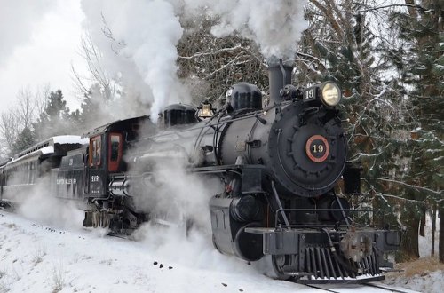 A vintage steam locomotive chugs through a snowy landscape, releasing clouds of steam into the cold air.