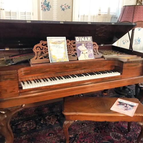 A vintage piano with sheet music and songbooks displayed on top, set in a cozy, decorated room.