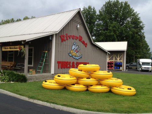 A stack of yellow river tubes in front of a building with a sign that reads "River Rat Tubes & Shuttle."