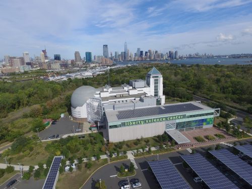 Aerial view of Liberty Science Center with skyline in the background, surrounded by greenery and solar panels.