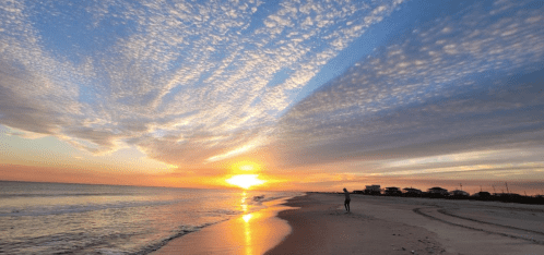 A serene beach at sunset, with vibrant clouds and a person walking along the shore.