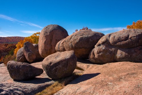 Large, rounded boulders scattered on a rocky surface, surrounded by autumn foliage under a clear blue sky.