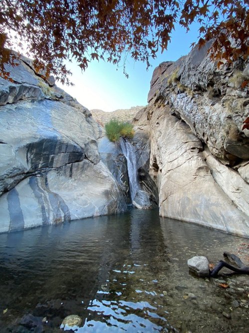 A serene waterfall cascades into a clear pool, surrounded by rocky cliffs and autumn foliage.
