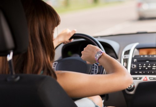 A person driving a car, glancing at their watch while holding the steering wheel.