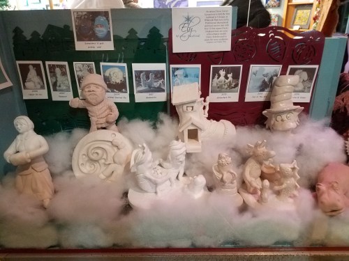 Display of whimsical sculptures in a snowy setting, featuring various characters and a cozy house.