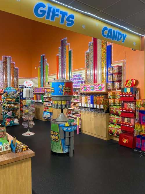 Colorful candy store interior with shelves of sweets, a candy machine, and a bright "Gifts" and "Candy" sign overhead.