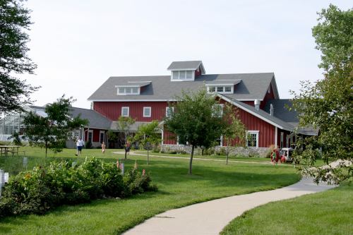 A red barn-style building surrounded by greenery and a pathway, with people walking in the area.