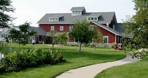 A red barn-style building surrounded by greenery and a pathway, with people walking in the area.