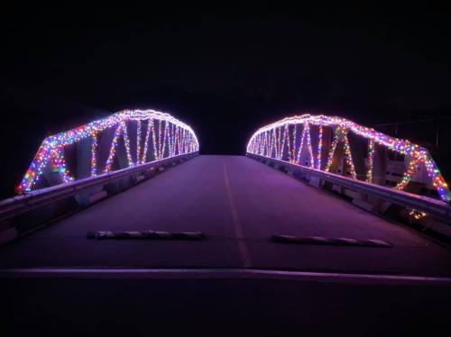 A brightly lit bridge adorned with colorful lights, set against a dark night sky.
