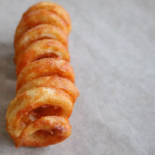 A crispy, golden-brown spiral potato fry on a parchment paper background.