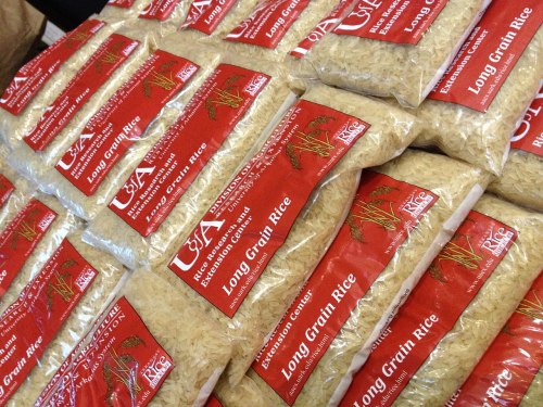 Bags of long grain rice stacked together, each with a red label featuring the brand name and product details.