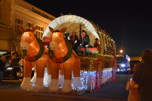A festive parade float featuring two large inflatable horses and riders, decorated with lights, at night.