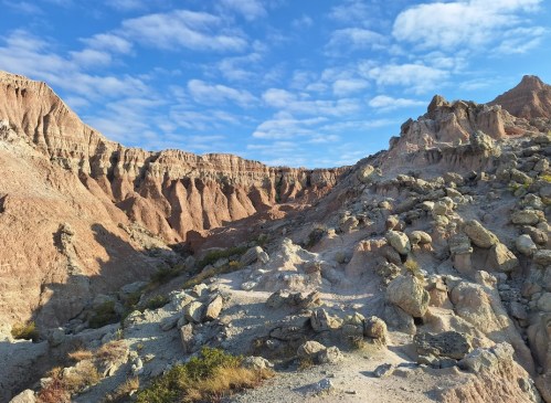 A rugged landscape of colorful rock formations and scattered boulders under a blue sky with fluffy clouds.