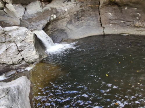 A small waterfall cascades into a dark pool surrounded by rocky terrain.