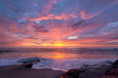 A vibrant sunset over the ocean, with colorful clouds reflecting on the water and gentle waves lapping at the shore.