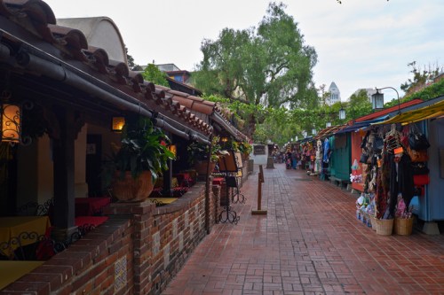 A charming brick pathway lined with colorful market stalls and rustic buildings under a cloudy sky.