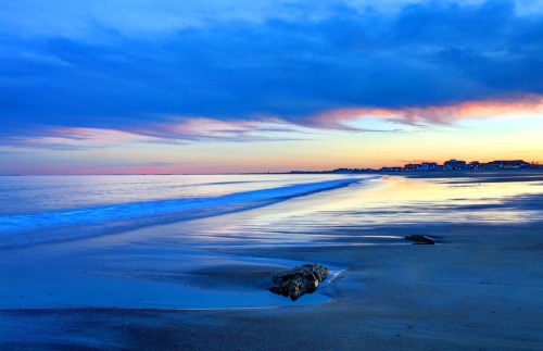 A serene beach at sunset, with gentle waves lapping at the shore and colorful clouds reflecting in the water.