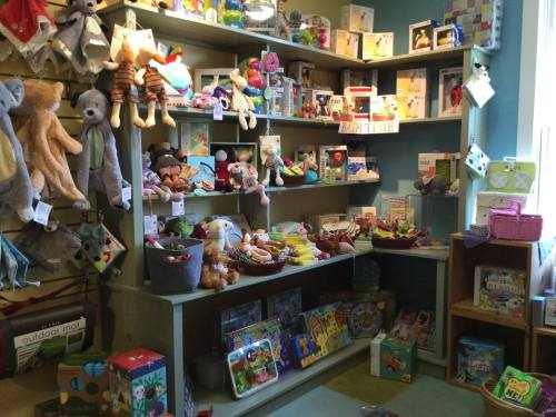 A colorful display of toys and stuffed animals on shelves in a cozy shop, featuring games, books, and baby items.
