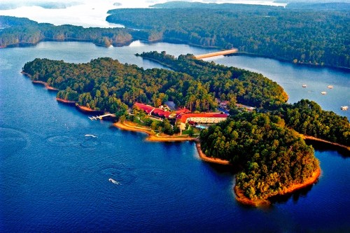 Aerial view of a lush green island surrounded by blue water, with a lodge and boats visible along the shoreline.