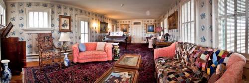 A cozy living room with patterned wallpaper, vintage furniture, a piano, and colorful rugs.