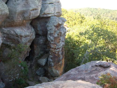 Rock formations surrounded by lush greenery and trees, with a clear blue sky in the background.