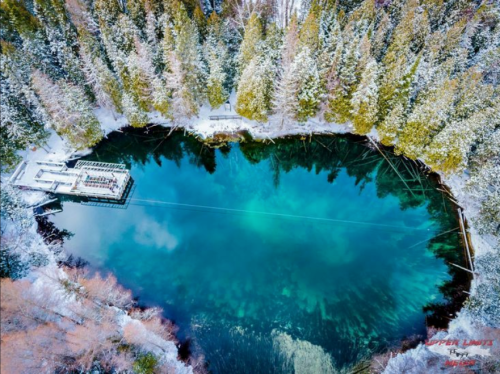Aerial view of a serene, turquoise lake surrounded by snow-covered trees and a small dock.