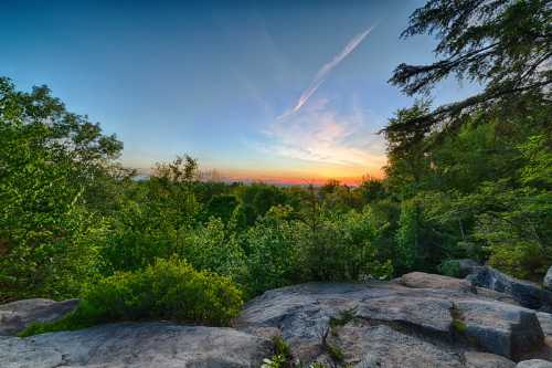 A vibrant sunset over a lush green landscape, with rocky outcrops and a clear blue sky.