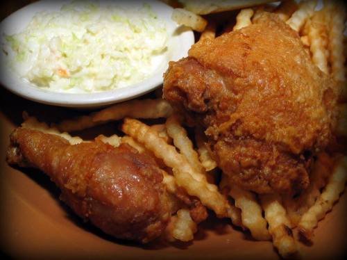 Fried chicken pieces served with crinkle-cut fries and a side of coleslaw on a brown plate.
