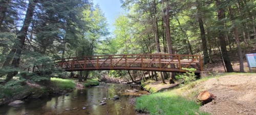 A wooden bridge spans a serene creek, surrounded by lush green trees and a peaceful natural landscape.
