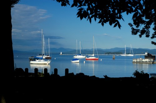 A serene lake scene with several sailboats anchored, surrounded by mountains and a clear blue sky.