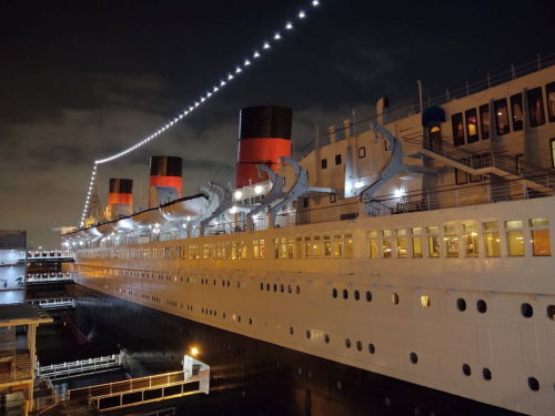 A historic ship illuminated at night, showcasing its iconic red and black smokestacks and deck lights.