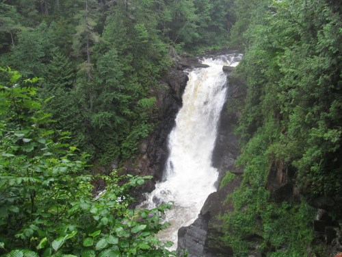 A cascading waterfall surrounded by lush green trees and rocky cliffs in a serene natural setting.