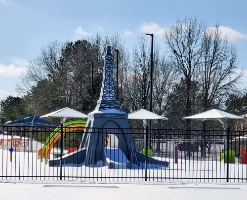 Playground featuring a blue Eiffel Tower slide surrounded by colorful play structures and snow-covered ground.