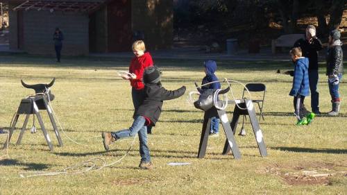 Children playing outdoors with toy horses, practicing roping skills in a grassy area.