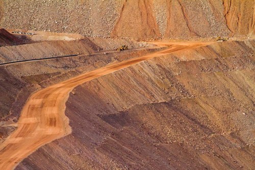 A winding dirt road cuts through a rocky landscape, with machinery visible in the distance.