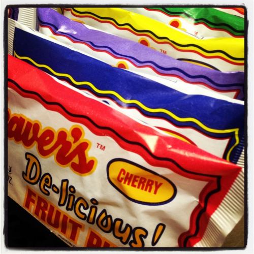Colorful fruit-flavored snack packages stacked, featuring cherry and other flavors with playful branding.